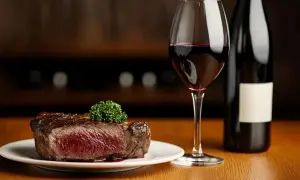 Un savoureux steak, un type de viande rouge juteuse, est servi avec un verre de vin rouge et une bouteille.