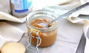 Un pot de confiture de lait onctueuse, une cuillère décorée et des biscuits sablés, prêts à être dégustés.