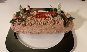 Bûche de Noël au chocolat, décorée de chantilly mascarpone, d'un Père Noël et de sapins dorés.