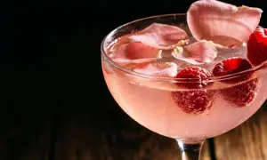 Cocktail rosé rafraîchissant garni de framboises et de pétales de rose. Une recette délicieuse pour l'été.