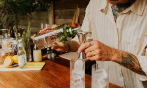 Un barman prépare un cocktail, versant du gin alcool de quoi dans un verre rempli de glaçons.