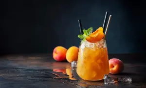 Un cocktail rafraîchissant au jus d'abricot alcool, garni d'une tranche d'abricot et de menthe, sur un lit de glace pilée.