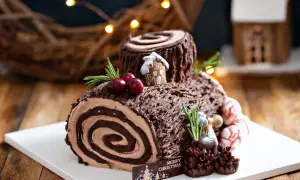 Bûche de Noël chocolatée, parfaite pour une recette génoise bûche moelleuse. Décorée de baies, romarin et d'une mini maison.
