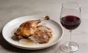 Un plat de canard rôti tranché, nappé de sauce, avec un verre de vin rouge. La question est : quel vin avec le canard ?