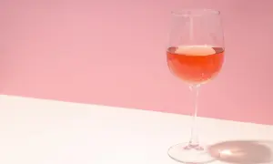 Verre de rosé très clair sur fond rose et blanc, avec une ombre projetée.