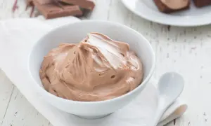 Un bol de namelaka chocolat onctueux, prêt à être dégusté. Des morceaux de chocolat sont visibles en arrière-plan.