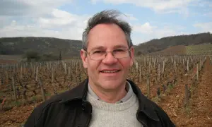 Alain Gras, souriant, se tient devant un vignoble vallonné.