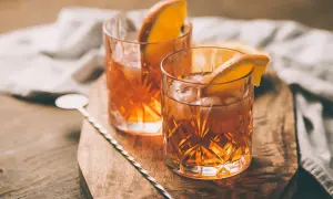 Deux verres d'armagnac digestif ambré, glacés et garnis d'une tranche d'orange, sur une planche en bois.