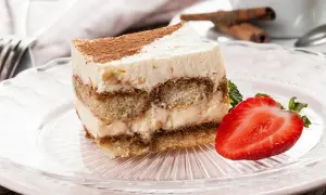 Tranche de tiramisu sans oeuf, garnie de cacao et d'une fraise fraîche, sur une assiette rose.