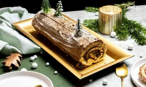 Une délicieuse recette de buche de Noel au chocolat, décorée de sapins miniatures et de neige, prête à être dégustée.