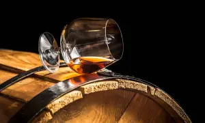 Verre de cognac renversé sur un tonneau en bois. Le liquide ambré suggère une question : le vin est-il un spiritueux ?
