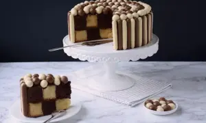 Un gâteau damier, décoré de bâtonnets et de billes chocolatées, présente une tranche coupée révélant ses couches alternées.