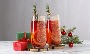 Deux verres de cocktail de Noël facile et rapide, décorés d'orange et de cannelle, avec des cadeaux et un sapin en arrière-plan.