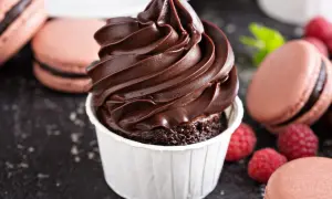 Un cupcake au chocolat surmonté d'une ganache montée chocolat au lait onctueuse, entouré de macarons et de framboises.