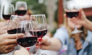 Des mains lèvent des verres de vin rouge pour un apéritif convivial.