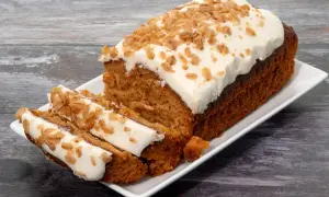Un délicieux gâteau carotte, généreusement glacé et parsemé de noix croquantes, est servi sur une assiette blanche.