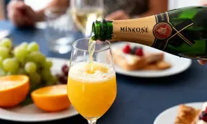 Une bouteille de Mimosé verse son contenu pétillant dans un verre rempli de jus d'orange, créant un cocktail mimosa parfait pour un brunch.