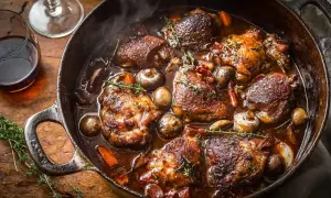 Un plat mijoté de coq au vin, avec des morceaux de poulet brunis, des champignons et des carottes dans une sauce riche. Le vin rouge parfait pour un coq au vin est ici !