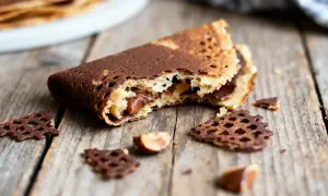 Un délicieux gâteau crêpe dentelle au chocolat, garni de noisettes, sur fond de bois rustique.