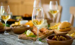 Verre de bordeaux blanc moelleux, parfait accompagnement pour crevettes, frites et mini-burgers sur une table rustique.