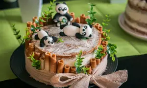 Un adorable layer cake anniversaire facile avec des pandas en pâte à sucre, des rouleaux de biscuit et des feuilles vertes.