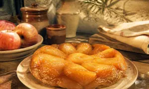 Une tarte tatin inratable, dorée et caramélisée, prête à être dégustée. Des pommes fraîches l'accompagnent.