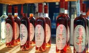 Plusieurs bouteilles de ratafia aux fruits rouges, dont le ratafia aux cerises et aux mûres, sont alignées sur une étagère en osier.