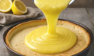 Une ganache citron onctueuse est versée dans une tartelette dorée. Des citrons frais sont visibles en arrière-plan.