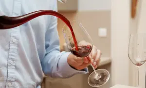 Un homme verse du vin rouge d'un **decanter ou carafer** dans un verre. Une autre bouteille et un verre vide sont visibles.