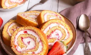 Tranches de gâteau roulé aux fraises et à la crème, parfaites pour une recette gâteau roulé facile. Une fraise coupée est posée sur l'assiette.