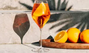 Un verre de Spritz pétillant, garni d'une tranche d'orange, avec des oranges fraîches sur un plateau. Parfait pour une recette spritz d'été.