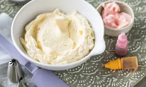 Crème au beurre à la meringue suisse onctueuse dans un bol blanc, avec des colorants et des douilles de pâtisserie.