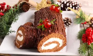 Un délicieux biscuit roulé moelleux au chocolat, décoré de cerises et de menthe, entouré de décorations de Noël.