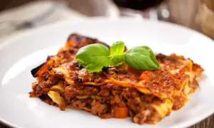 Une part de lasagne savoureuse, garnie de basilic frais, parfaite avec un verre de vin rouge.