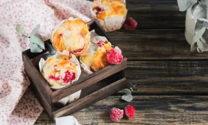 Muffins framboise dorés et moelleux dans une caisse en bois, décorés de quelques framboises fraîches.