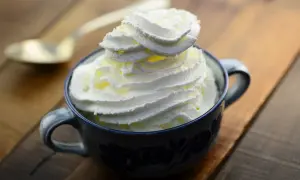Une tasse de chantilly maison, aérienne et onctueuse, prête à être dégustée. Une cuillère dorée est posée à côté.