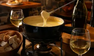 Une belle quantité de vin blanc accompagne une fondue savoyarde fumante, prête à être dégustée avec du pain croustillant.
