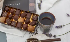 Boîte de chocolats Louvins, dont une ganache praliné, avec une tasse de café et des brins de lavande.
