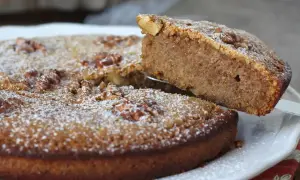 Gâteau aux noix, saupoudré de sucre glace. Une part est soulevée, révélant la texture moelleuse de cette recette de noix.