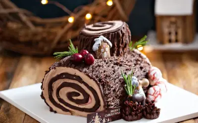 Bûche de Noël chocolatée, parfaite pour une recette génoise bûche moelleuse. Décorée de baies, romarin et d'une mini maison.