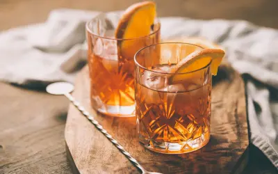 Deux verres d'armagnac digestif ambré, glacés et garnis d'une tranche d'orange, sur une planche en bois.