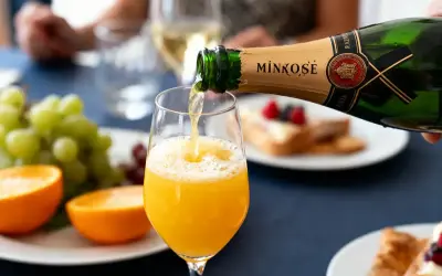 Une bouteille de Mimosé verse son contenu pétillant dans un verre rempli de jus d'orange, créant un cocktail mimosa parfait pour un brunch.