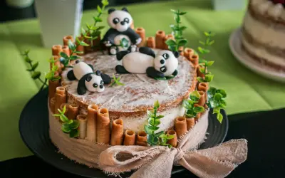 Un adorable layer cake anniversaire facile avec des pandas en pâte à sucre, des rouleaux de biscuit et des feuilles vertes.