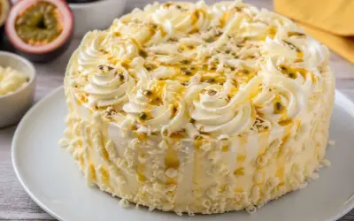 Un délicieux gâteau blanc orné de crème fouettée, de fruits de la passion et de copeaux de chocolat blanc.