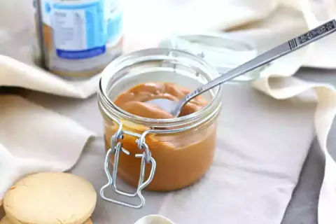 Un pot de confiture de lait onctueuse, une cuillère décorée et des biscuits sablés, prêts à être dégustés.