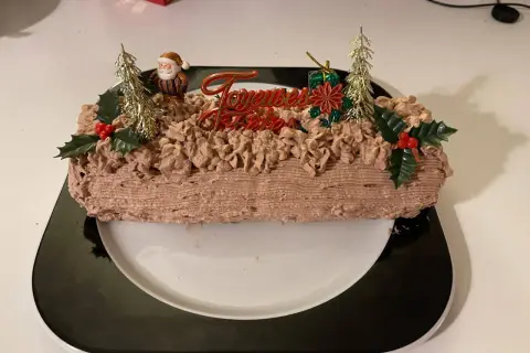 Bûche de Noël au chocolat, décorée de chantilly mascarpone, d'un Père Noël et de sapins dorés.