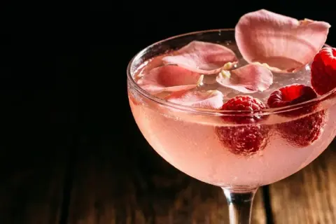 Cocktail rosé rafraîchissant garni de framboises et de pétales de rose. Une recette délicieuse pour l'été.