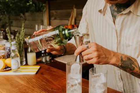 Un barman prépare un cocktail, versant du gin alcool de quoi dans un verre rempli de glaçons.