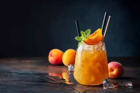 Un cocktail rafraîchissant au jus d'abricot alcool, garni d'une tranche d'abricot et de menthe, sur un lit de glace pilée.