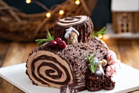 Bûche de Noël chocolatée, parfaite pour une recette génoise bûche moelleuse. Décorée de baies, romarin et d'une mini maison.